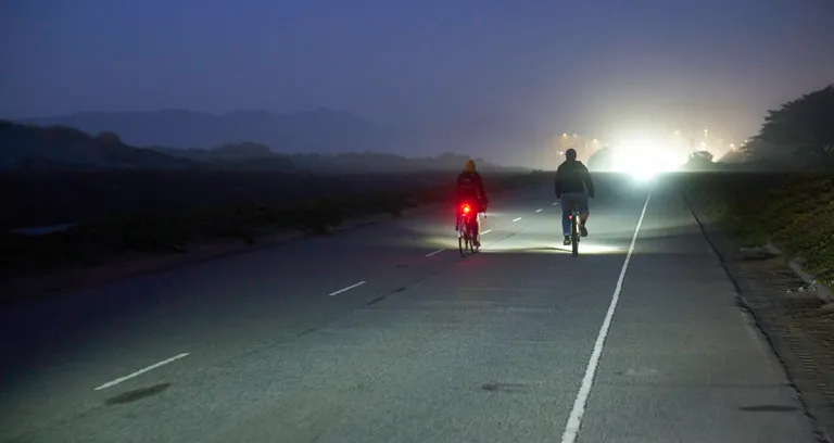 Kat and Connor riding away from the camera at Ocean Beach Park in the dark, with a bright light shining in front of them.