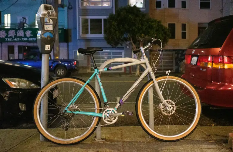 The bike leaning against a bike rack outside at night in its nearly complete state.