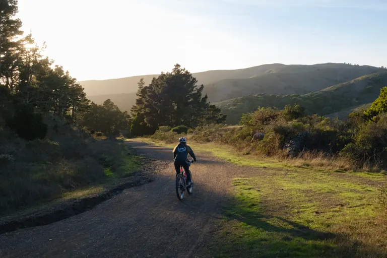 Kat on her bike descending down a wide gravel trail into the sunset.