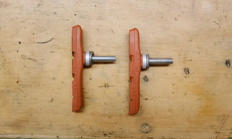 Two threaded cantilever brake pads sitting on a bench. They both have their concave/convex washer pairs but one has an additional 1mm spacer.