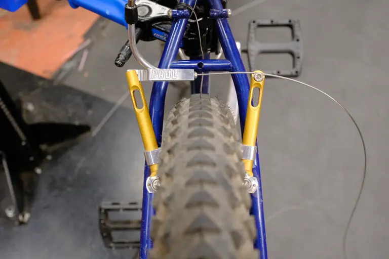 A view of the rear brake with an improved clearance between cable guide and top of tire, and with the brake arms further tucked into the frame.
