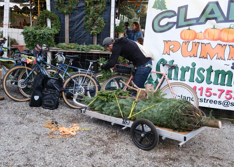 Ben adjusting a wreath on his bike basket behind the 6 foot trailer with a tree and reindeer decoration on it