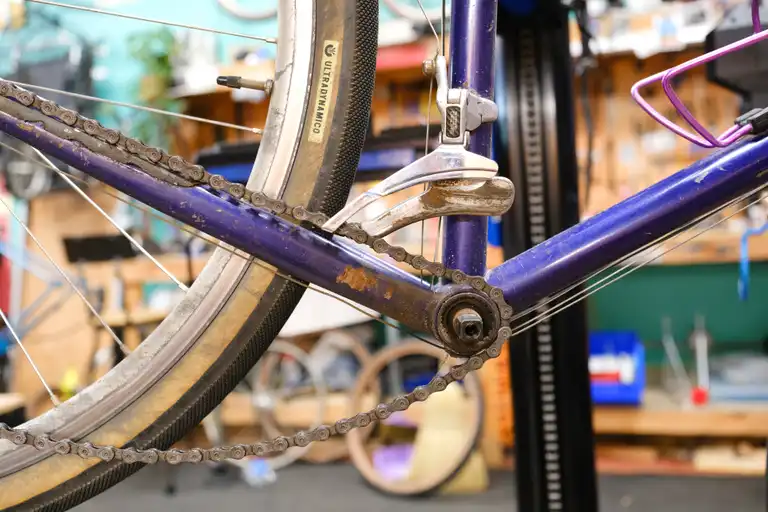 The bottom bracket and rusty purple chainstay of a 1992 Trek. A chain is hanging over the bottom bracket shell without a crank on.