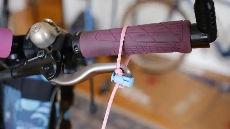 A pink and blue brake lock made from paracord securing a brake lever to a grip.