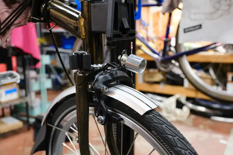 A cylindrical light mount attached to the reflector bracket on the fork crown of a Brompton.