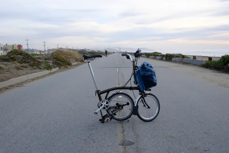 A Brompton with the rear frame folded under in the middle of a road with dramatic clouds behind it.