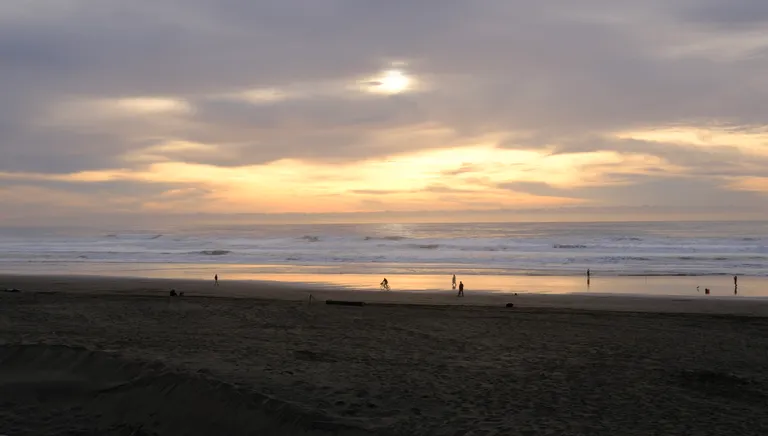Looking out at the Pacific Ocean at golden hour with the low sun poking through the clouds a bit. There's someone biking through the sand on Ocean Beach.