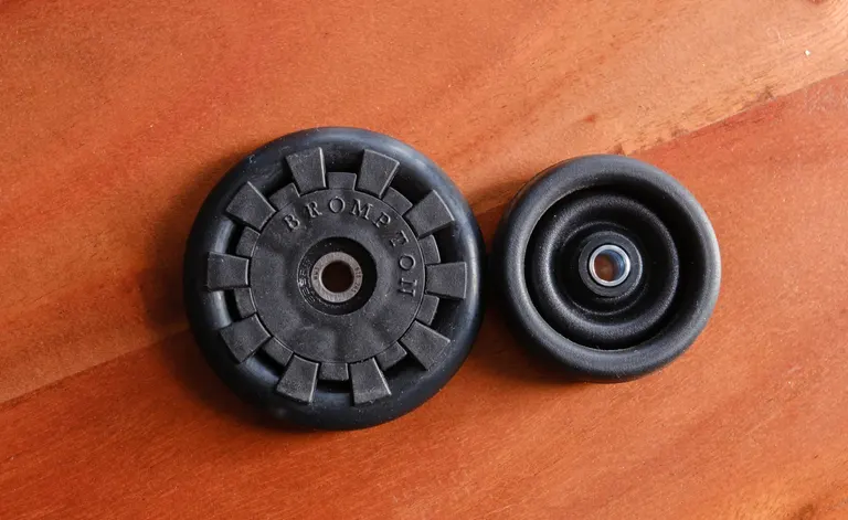 Looking top-down at a small black eazy wheel on the left beside a smaller black stock wheel on the right. The left one says 'Brompton'.