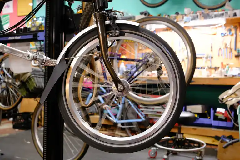 A spinning front dynamo wheel on a small Brompton fork hanging in a bike stand. No wiring or lights yet.