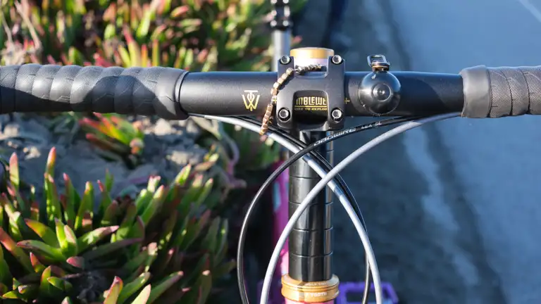 A close-up view of a bike stem on top of many big headset spacers. There's black bar tape and a black bar with gold accents.