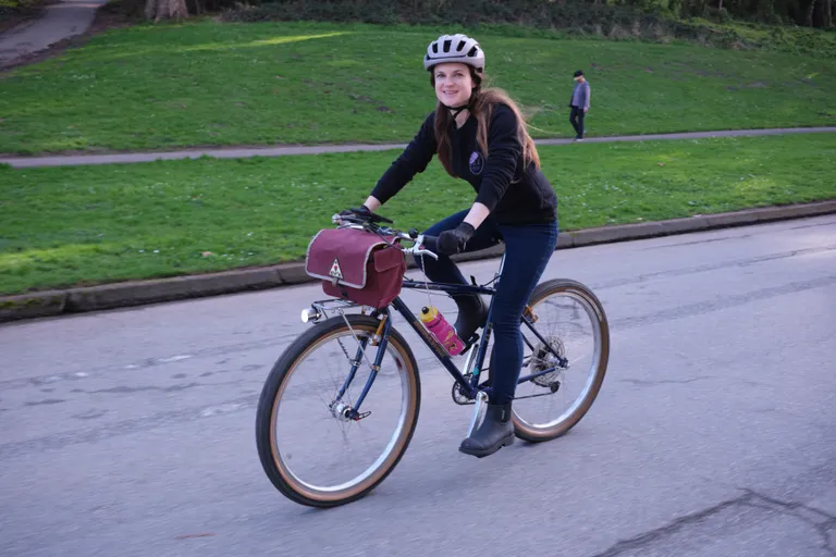 Kat biking on her blue and gold BB-1 with a Fabs Fanny in front, smiling at the camera