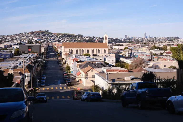 A vista of a church, hills, and a distant San Francisco skyline from the top of a hill