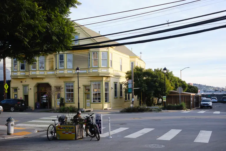 A yellow building on the corner of an intersection with a bench on the other side