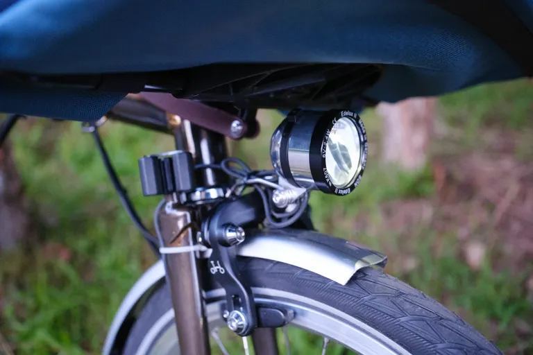 A close up of an Edelux II dynamo light mounted above the front wheel of a Brompton.