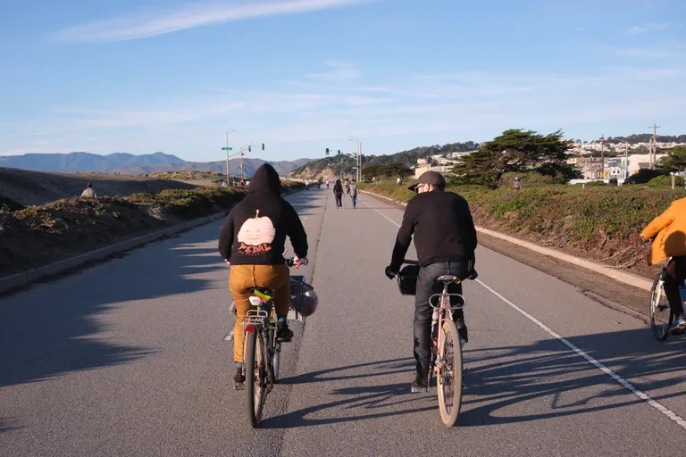 Sarah biking in a 'Pedal Revolution' hoodie beside Ben