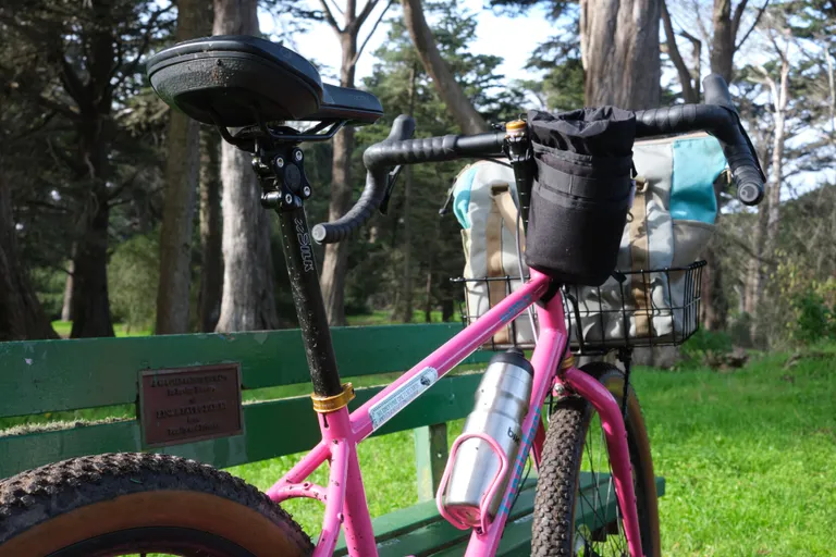 The upper half of a muddy pink bike resting against a bench