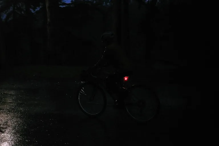 Kat biking in the rain, very dark, hard to see her, some raindrops illuminated