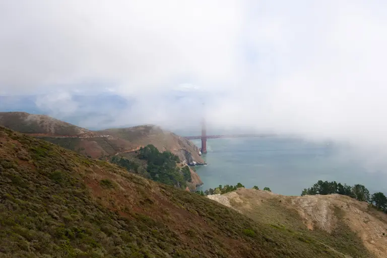 The Golden Gate Bridge nearly covered by fog behind the Marin headlands hills