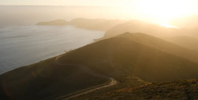 The sun over Marin hills next to the Pacific ocean with a winding road