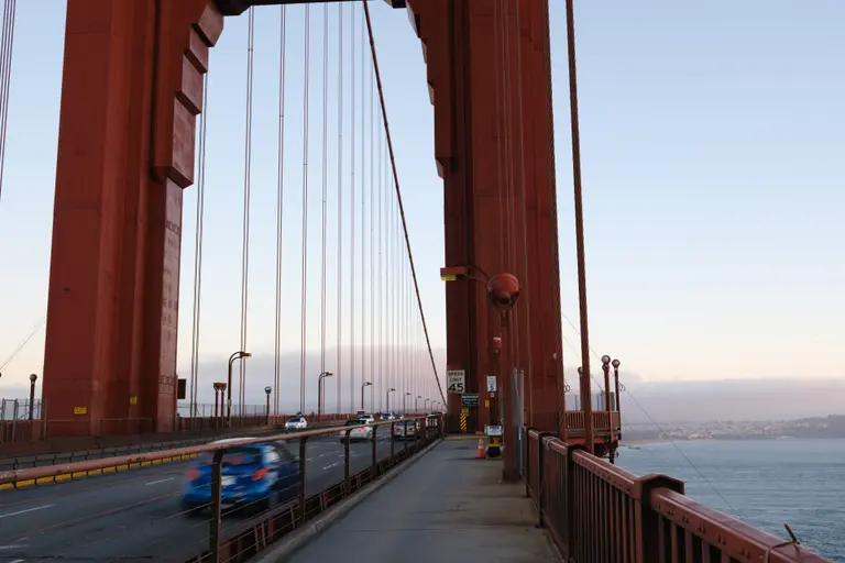 A bike path on the golden gate bridge with motion blurred cars on the left and the Pacific ocean on the right
