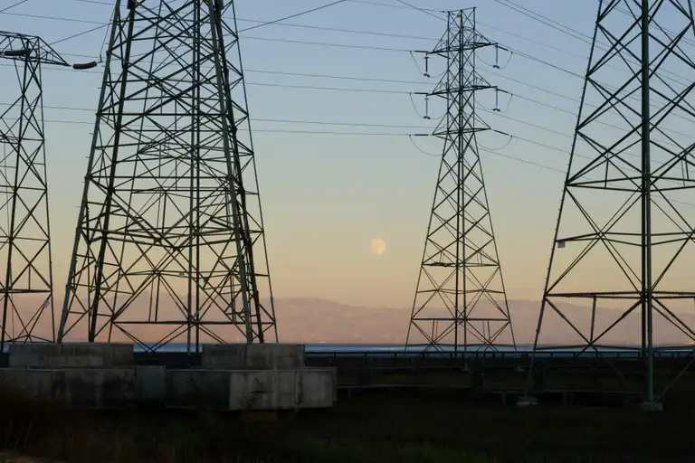 A nearly full moon at golden hour between a bunch of electricity towers