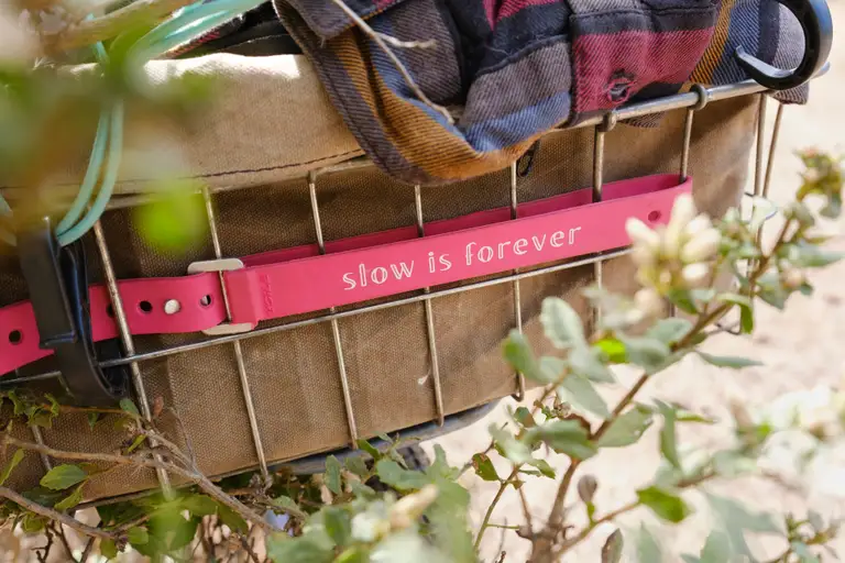 A magenta voile strap around a basket that reads 'Slow is Forever'