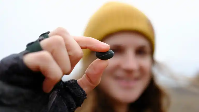 Kat holding a small, smooth, dark pebble with a single stripe