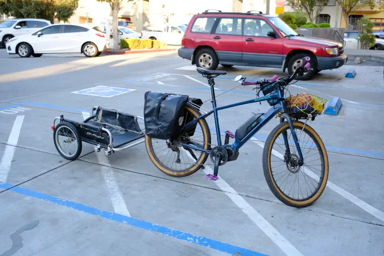 A blue e-bike in a parking space with a Burley trailer hitched to its back