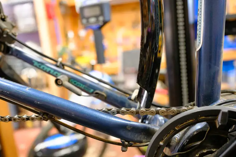 The chainstay bridge of a blue bike with the rear wheel removed showing just the black fender being setup. The bottom edge of the fender is slightly warped