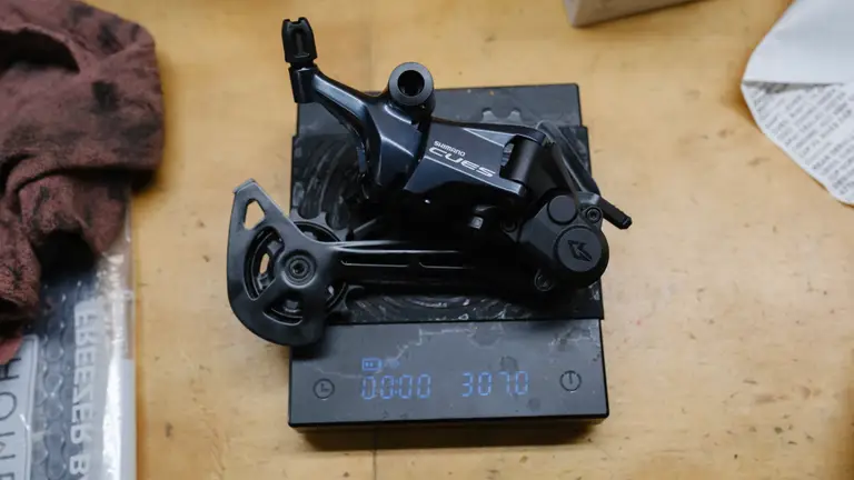 A derailleur with the faceplate reading 'Shimano Cues' on a coffee scale reading 307.0g