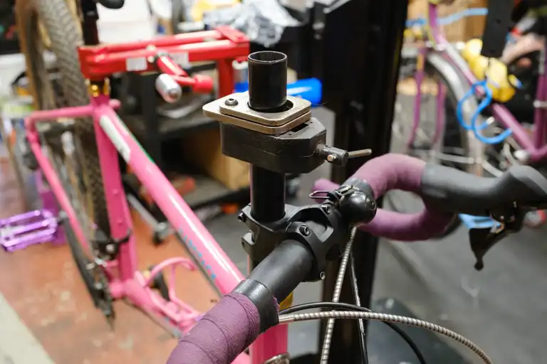 The threadless steerer tube of a pink bike with a cutting guide clamped onto the steerer