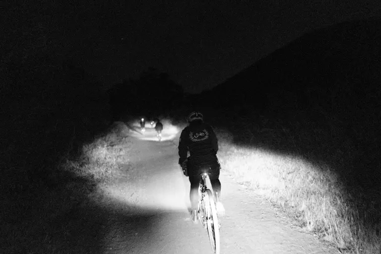 Kat riding in the dark toward Bobcat Trail with multiple riders up a bit in the distance