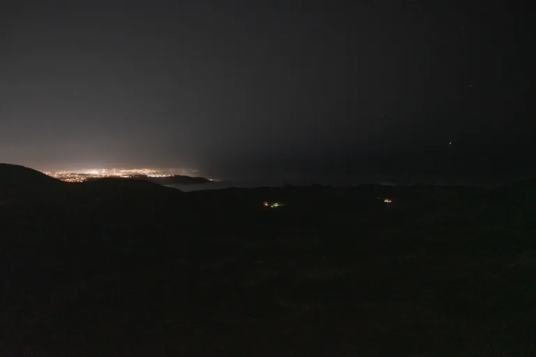 A view of the ocean and west side of the city in the dark from near the top of Bobcat Trail. There are some stars and a glow from the city
