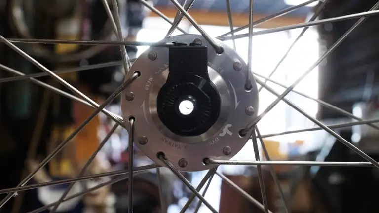 The drive side of a laced dynamo hub with light shining through the hollow axle. There's a small lip inside the axle.