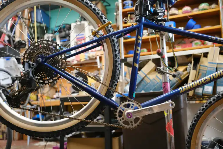 A blue and gold bike in a bike stand with polished silver cranks, a black cassette, and a black derailleur installed.
