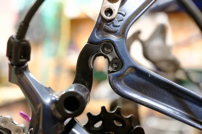 A black derailleur hanger installed in a blue frame. There's marring from the skewer flange.
