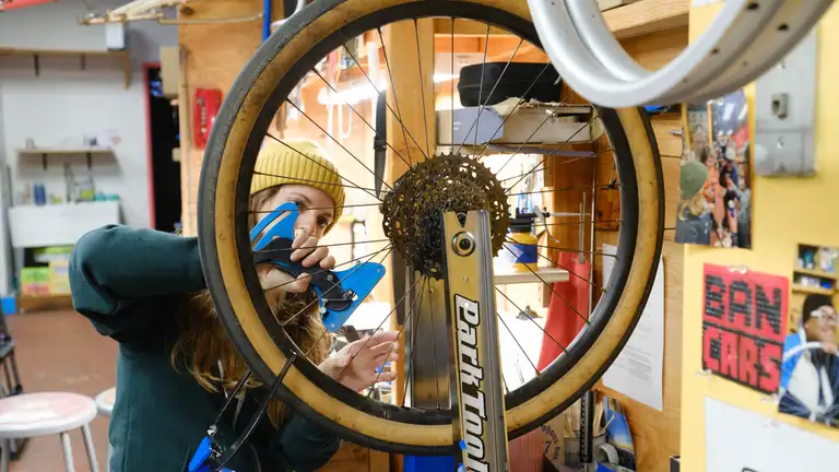 A wheel in a truing stand with a person standing behind it with a tension meter.