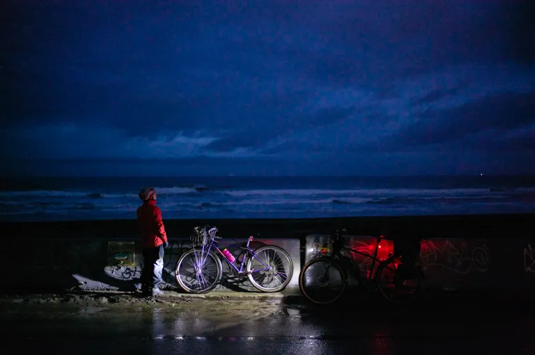 Kat looking at a moody sky in dim light with her Trek and my Kona resting against a barrier
