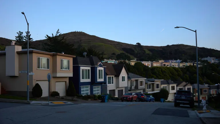 A suburban intersection with colorful homes and one half of Twin Peaks in the background