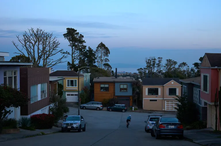 A biker going down a steep road into a turn around colorful suburbn homes at blue hour
