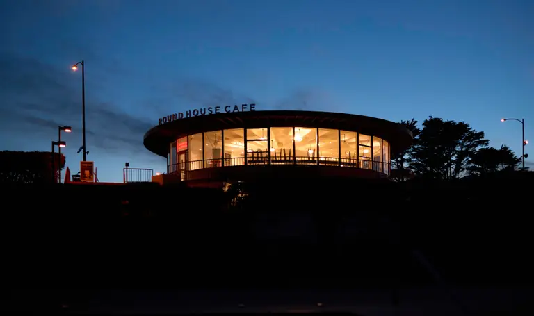 A cylindrical shaped building with a sign that reads 'Round House Cafe', at dusk