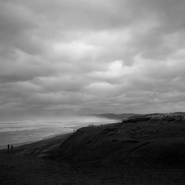 Black-and-white photo of the beach and sand dunes near Sloat looking towards very low lying fog and clouds