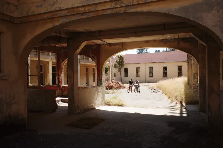 Looking through an abandoned building on Angel Island to a sunnier spot with two cyclists standing over their bikes.