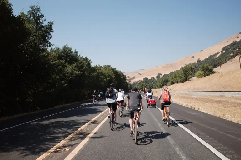 Multiple bike riders in each direction on a highway without a car facing the distant hills