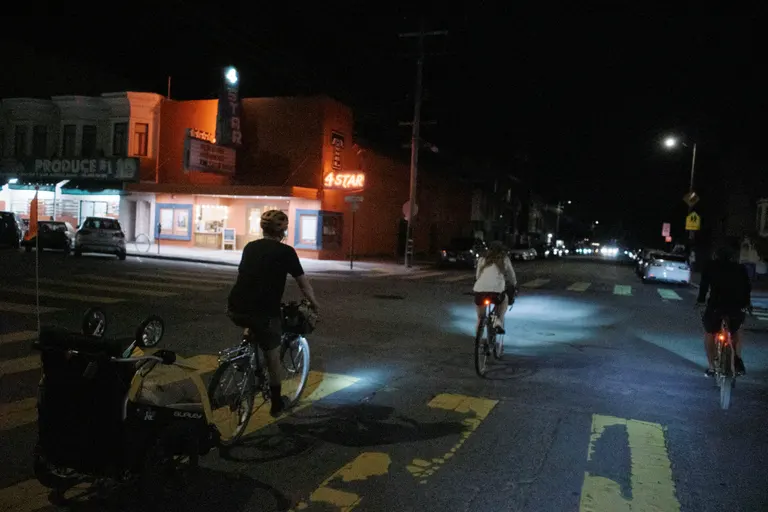 Three people on bicycles entering an intersection crossing the 4 star theatre.