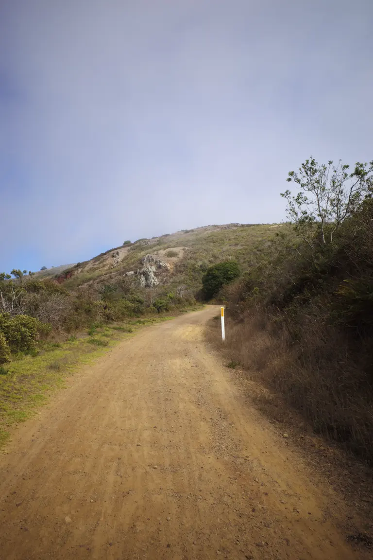 A curvy uphill trail showing the bushy and rocky hills of the Marin Headlands.