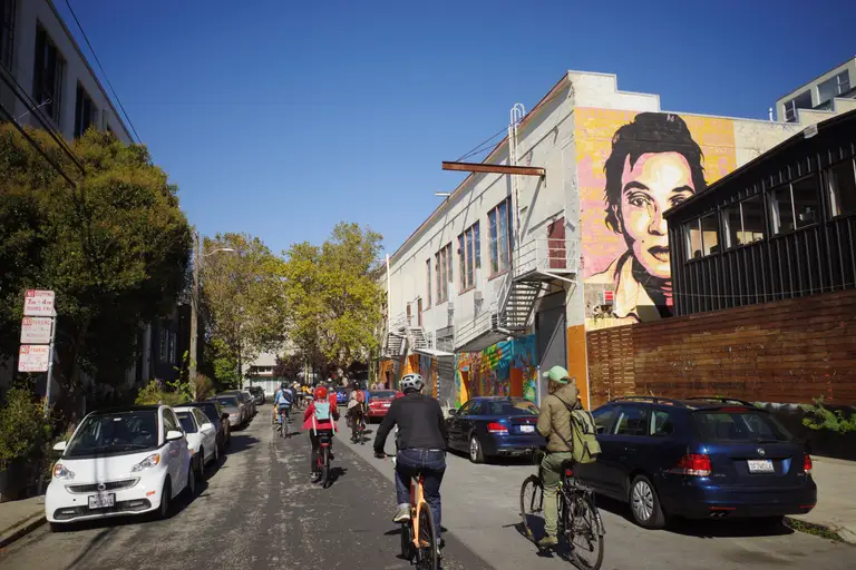 A group of cyclists riding towards a turn surrounded by colorful murals.