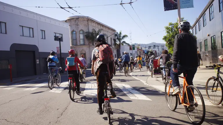 A group of cyclists riding around a turn with a 'Mission Creek' banner on the right.
