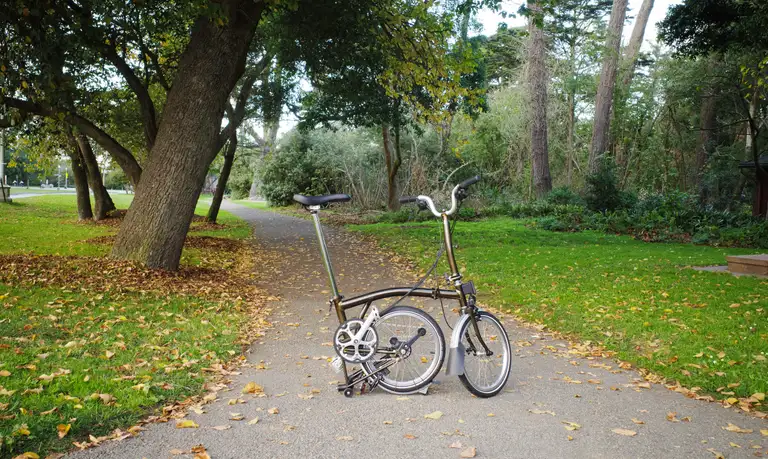 A Brompton on a wooded path with its rear triangle folded up in 'parking' position.