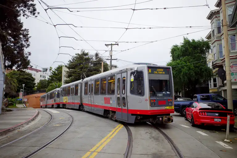 A Muni train going around a turn. An array of wires above and a tunnel in the background. The headbadge reads 'N Judah Caltrain'.